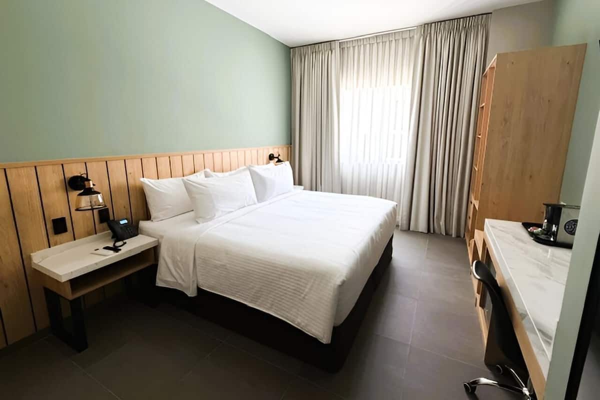 A hotel room with a bed, bedside table, lamp, and a wooden wardrobe.