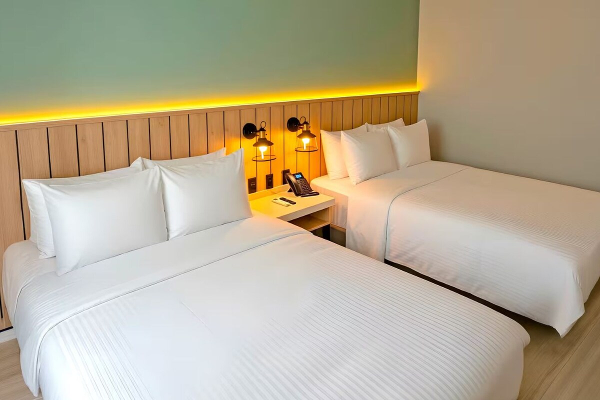 Une chambre d’hôtel avec deux lits, une tête de lit en bois et des lampes de chevet.