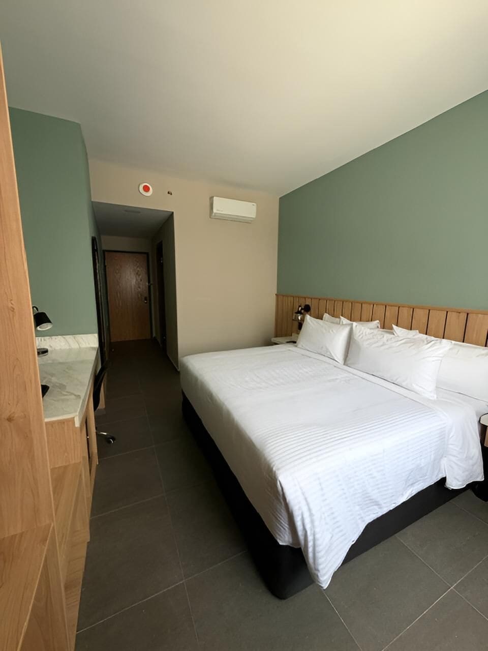 Habitación de hotel con cama, un escritorio de madera, una mesita de noche y una puerta que da a otra habitación.