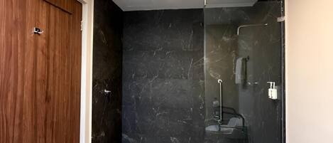 Una habitación con puerta de madera, cabina de ducha de vidrio y una lámpara de techo blanca.