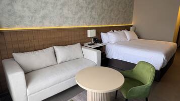 A hotel room with a bed, a sofa, a small table, and two chairs.