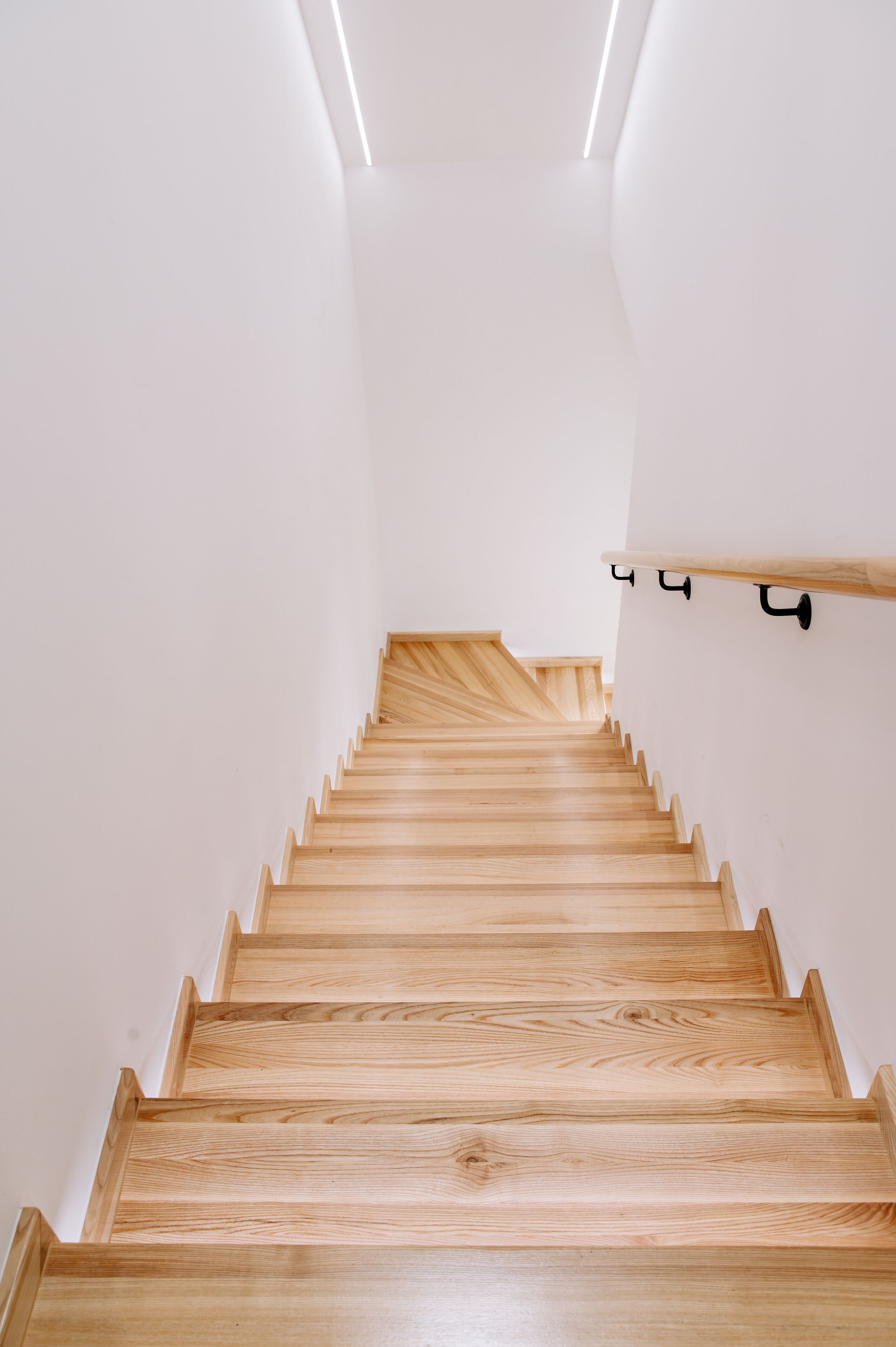 A wooden staircase with a handrail and a light fixture above.