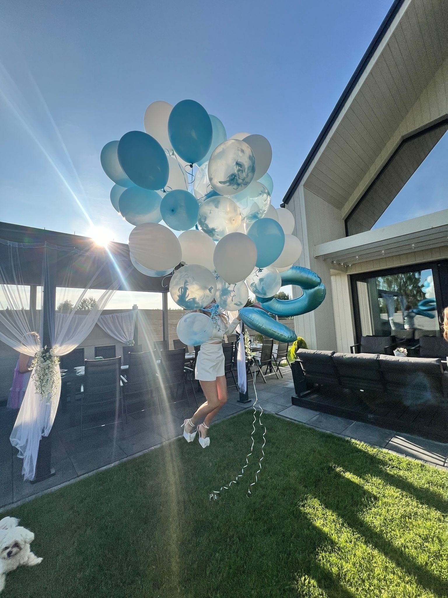 A person holding a cluster of balloons outdoors with a building in the background.