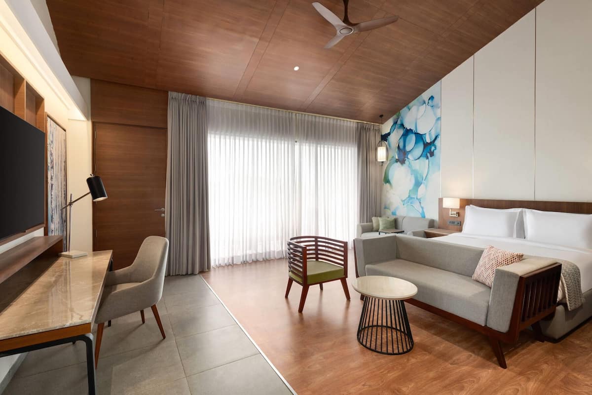A modern hotel room with a wooden ceiling, a large bed, a sofa, a dining table, and a TV.
