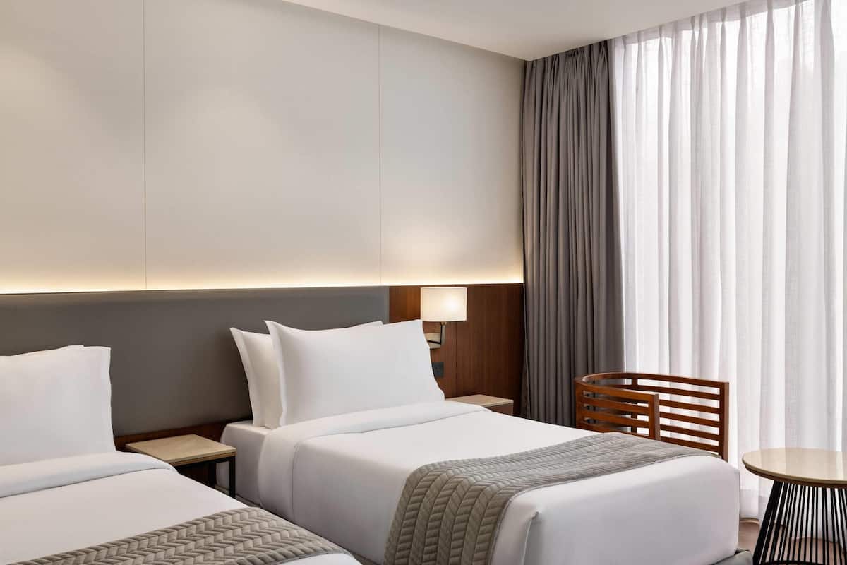 A hotel room with two beds, a wooden chair, a small table, and a large window with curtains.