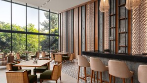 A modern restaurant with large windows, wooden furniture, and decorative panels.