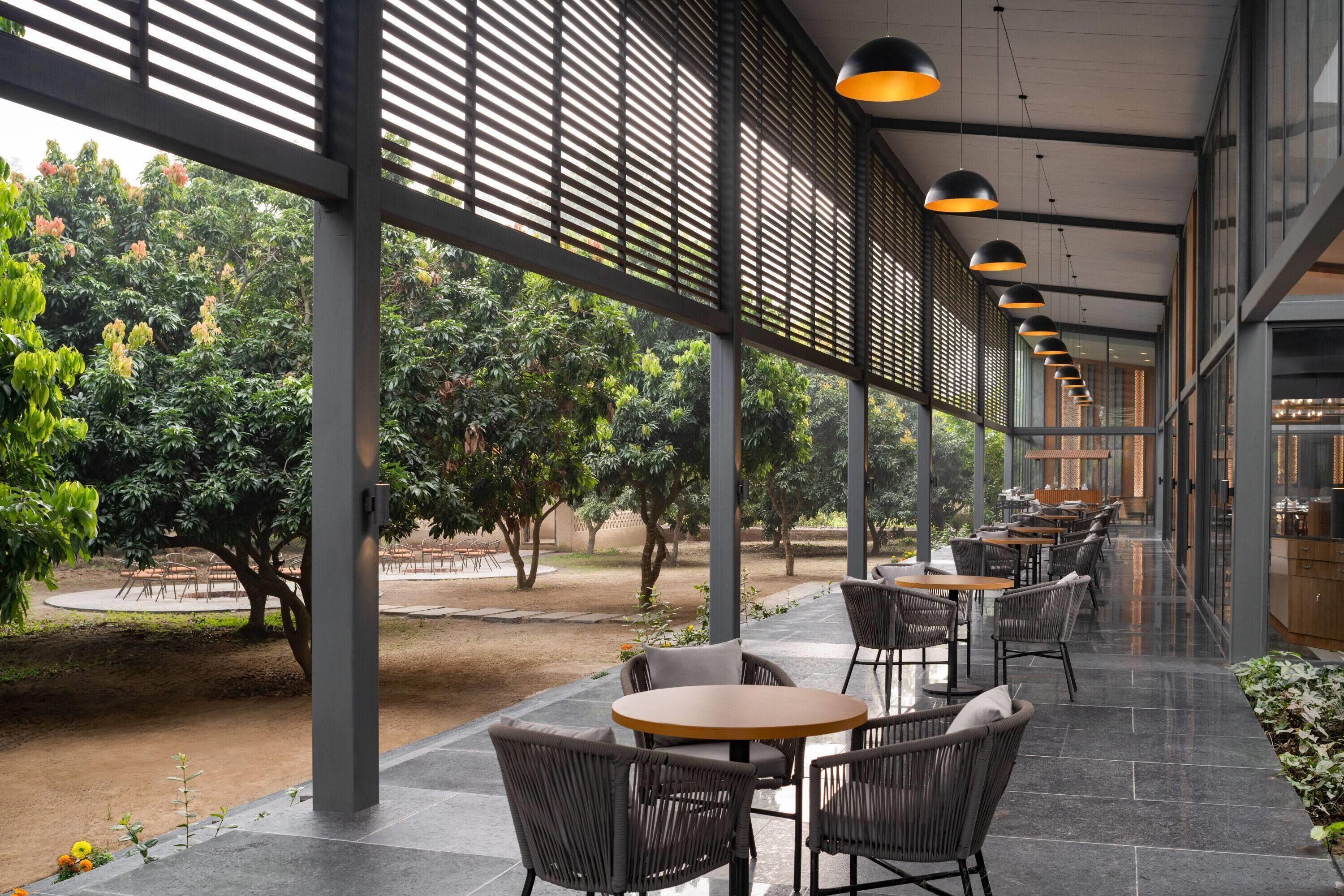 An outdoor café area with tables and chairs, surrounded by a garden with trees and plants.