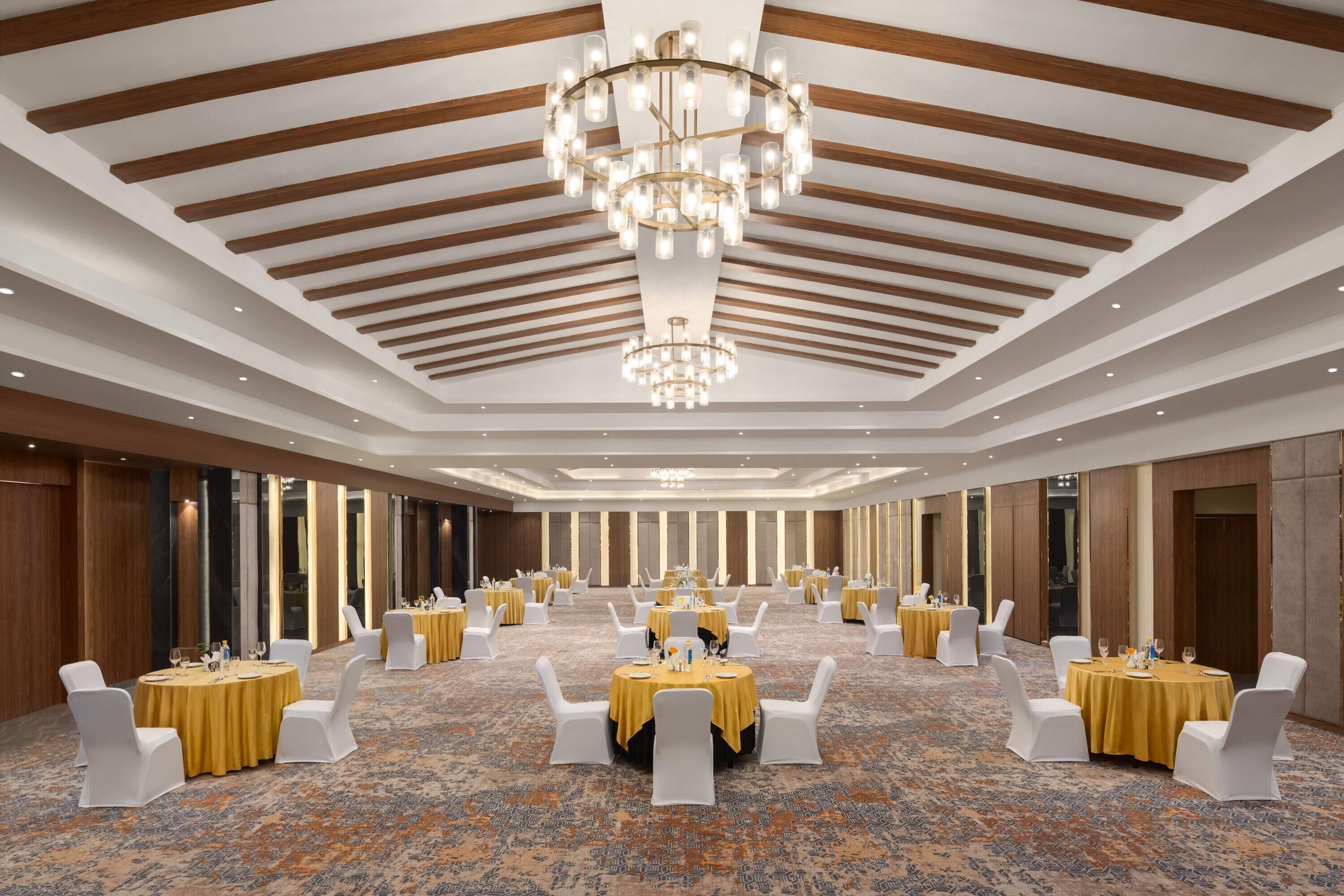 Un salón de banquetes con mesas redondas, sillas blancas y una araña de cristal.
