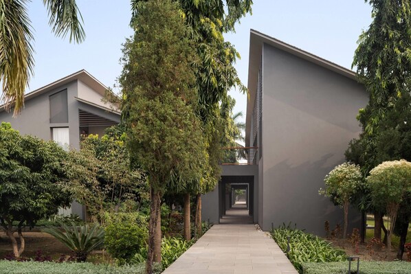A modern building with a central pathway flanked by lush greenery and trees. - Wyndham Garden JIM Corbett Chhoi (Ramnagar)
