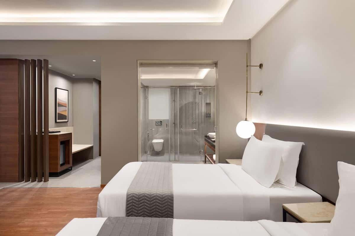 A modern hotel room with a large bed, bedside tables, a desk, and a shower area.