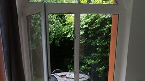 Une véranda avec une table et des chaises blanches, une porte vitrée donnant sur un espace extérieur équipé d’une table et de chaises.