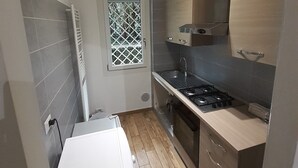Une cuisine compacte équipée d’une cuisinière à gaz, d’un four encastré et d’une fenêtre ornée d’un motif en treillis.