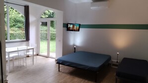 Une chambre à coucher comprenant un lit, un téléviseur fixé au mur, un bureau avec des chaises et une porte-fenêtre coulissante donnant sur un jardin.
