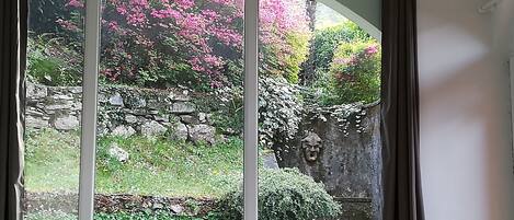 A view through a large arched window with a stone wall and flowering plants.