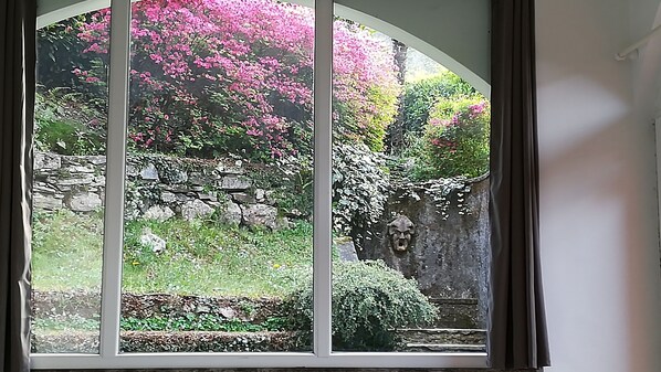 A view through a large arched window with a stone wall and flowering plants.