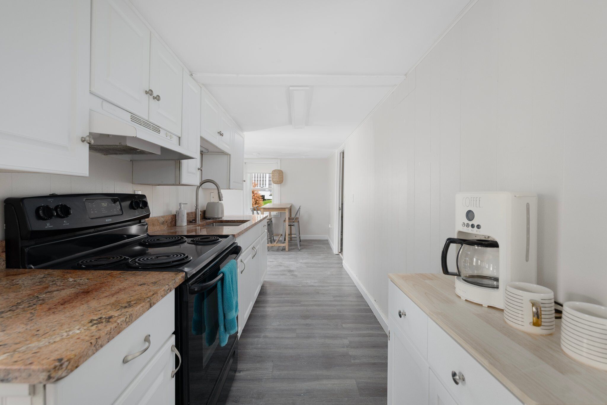 Una cocina moderna con armarios blancos, encimera de granito, estufa negra y cafetera.