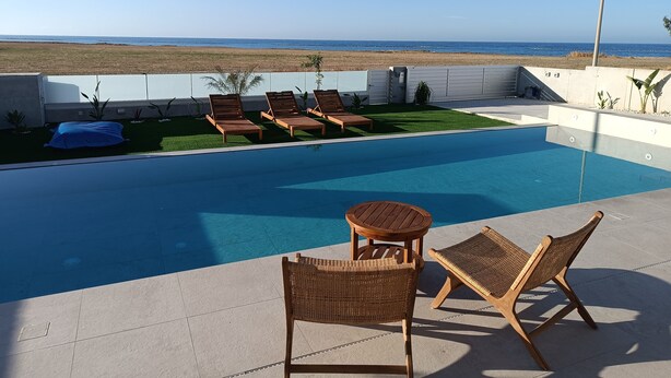 A swimming pool with lounge chairs and a table on a patio with a view of the ocean.
