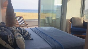 A bedroom with a large bed, a view of the beach, and a balcony with a chair.