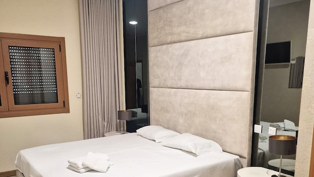 A modern bedroom with a large bed, a bedside table, a mirror, and a window with blinds. - Modern Lisbon Apartment (Odivelas)