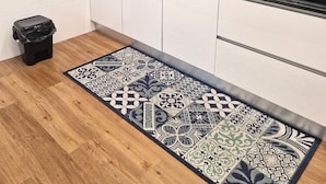 A modern kitchen with white cabinets, a black countertop, and a patterned rug. - Modern Lisbon Apartment (Odivelas)