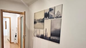 A hallway with wooden flooring and a wall with a series of landscape paintings. - Modern Lisbon Apartment (Odivelas)