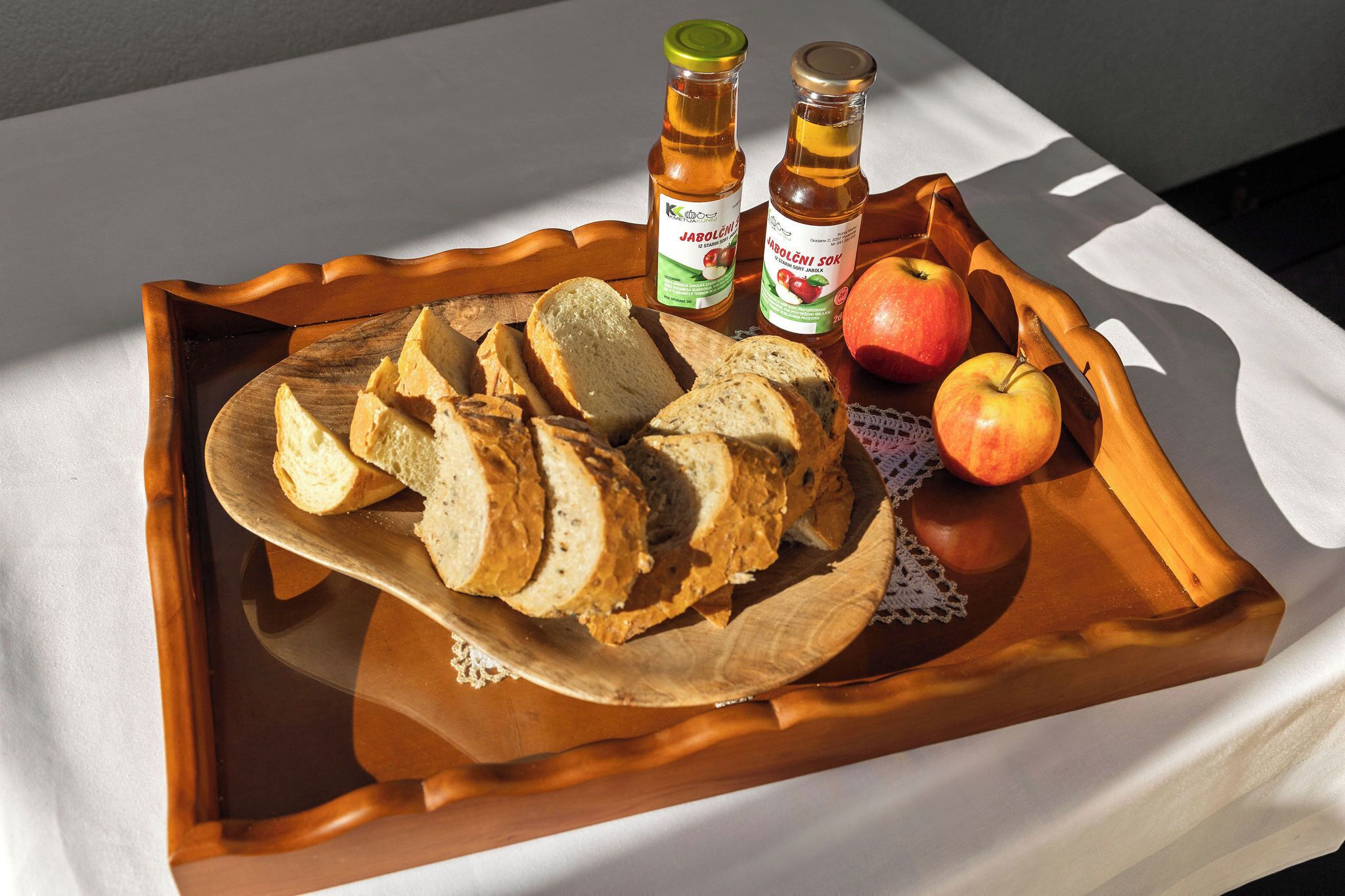 Ein Holztablett mit Scheibenbrot, einem ganzen Apfel und zwei Flaschen Jablonec-Sirup.