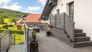 Una terraza moderna al aire libre con una escalera que lleva a un segundo piso, rodeada de vegetación y vistas a una ladera.