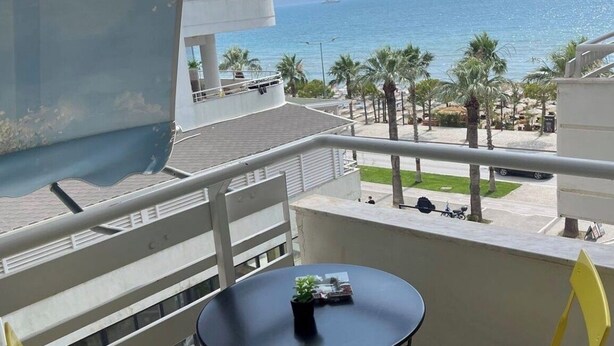 A balcony with a table and chairs, overlooking a beach with palm trees and a clear view of the sea. - Seaside retreat with stunning sea views – steps from the beach, pure relaxation. (Vlore)