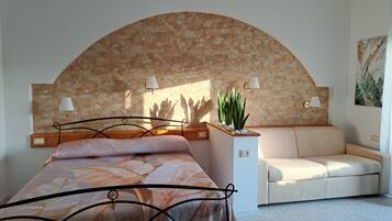 Ein Schlafzimmer mit einer Steinkonstruktion, einem Bett mit floralem Überwurf, einem Nachttisch mit Lampe und einem Sofa.