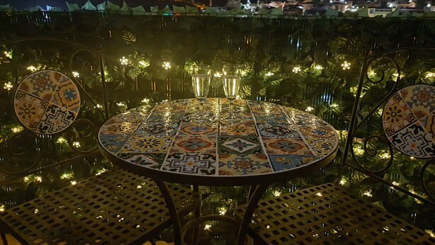 Ein runder Tisch mit Mosaikfliesenmuster, umgeben von Stühlen mit einem Metallgitterdesign.