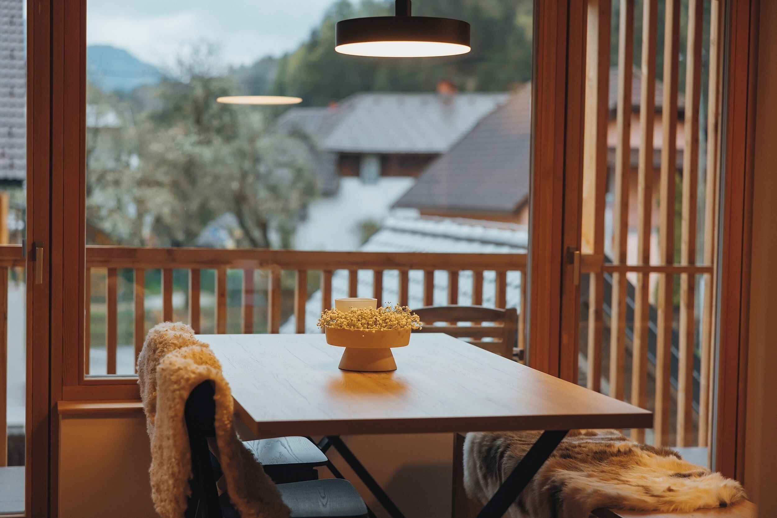 A wooden table with a bowl of flowers on a balcony overlooking a snowy landscape.