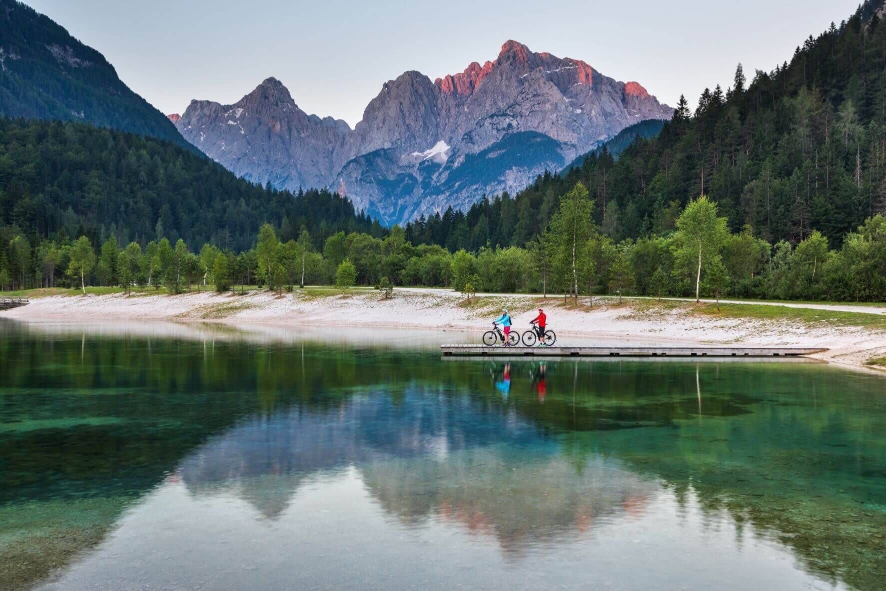 A lake with clear water reflecting the surrounding mountains and trees.