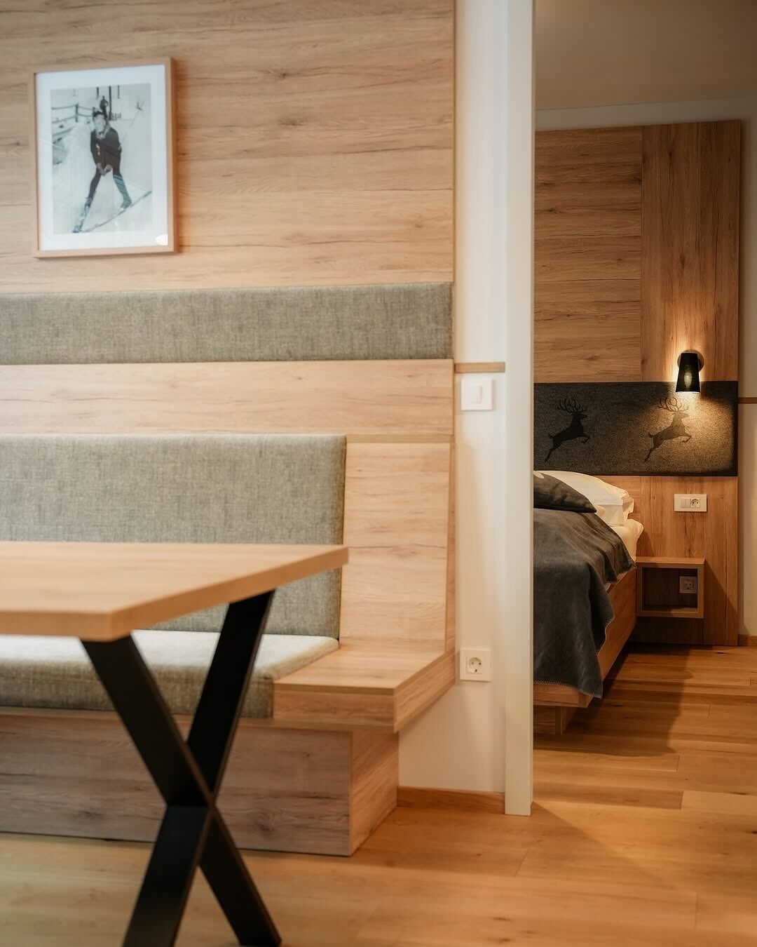 A modern bedroom with a wooden floor, a bed with a headboard, a bedside table, and a wall-mounted light fixture.