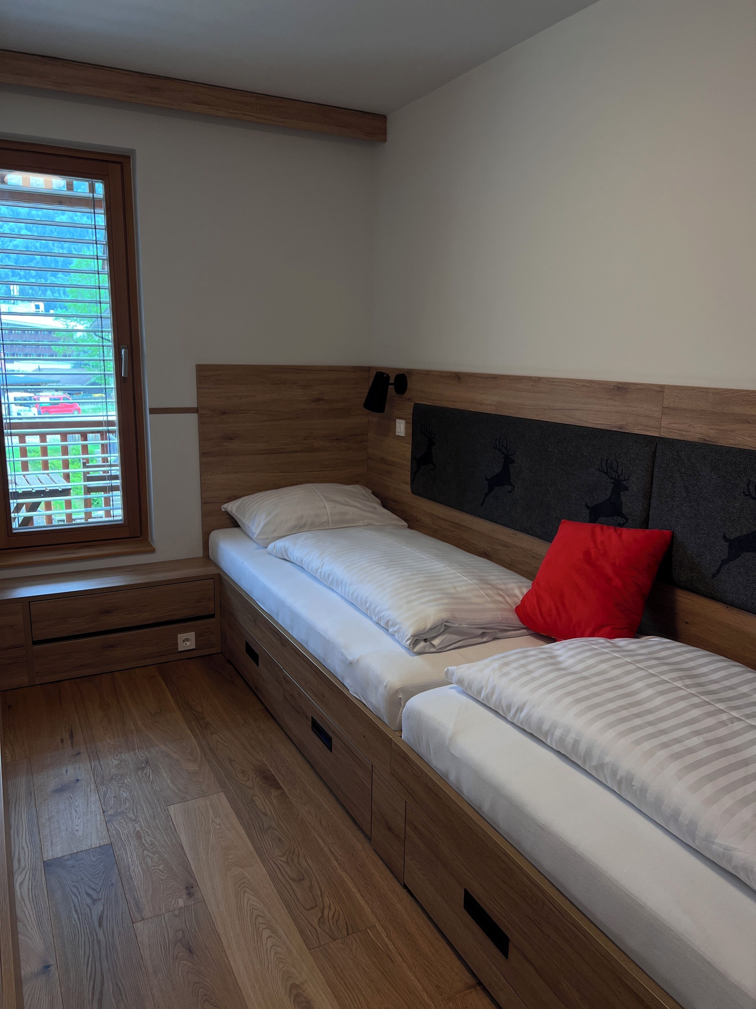 Camera da letto con testiera in legno, una finestra con persiane e un letto con biancheria bianca e un cuscino rosso.