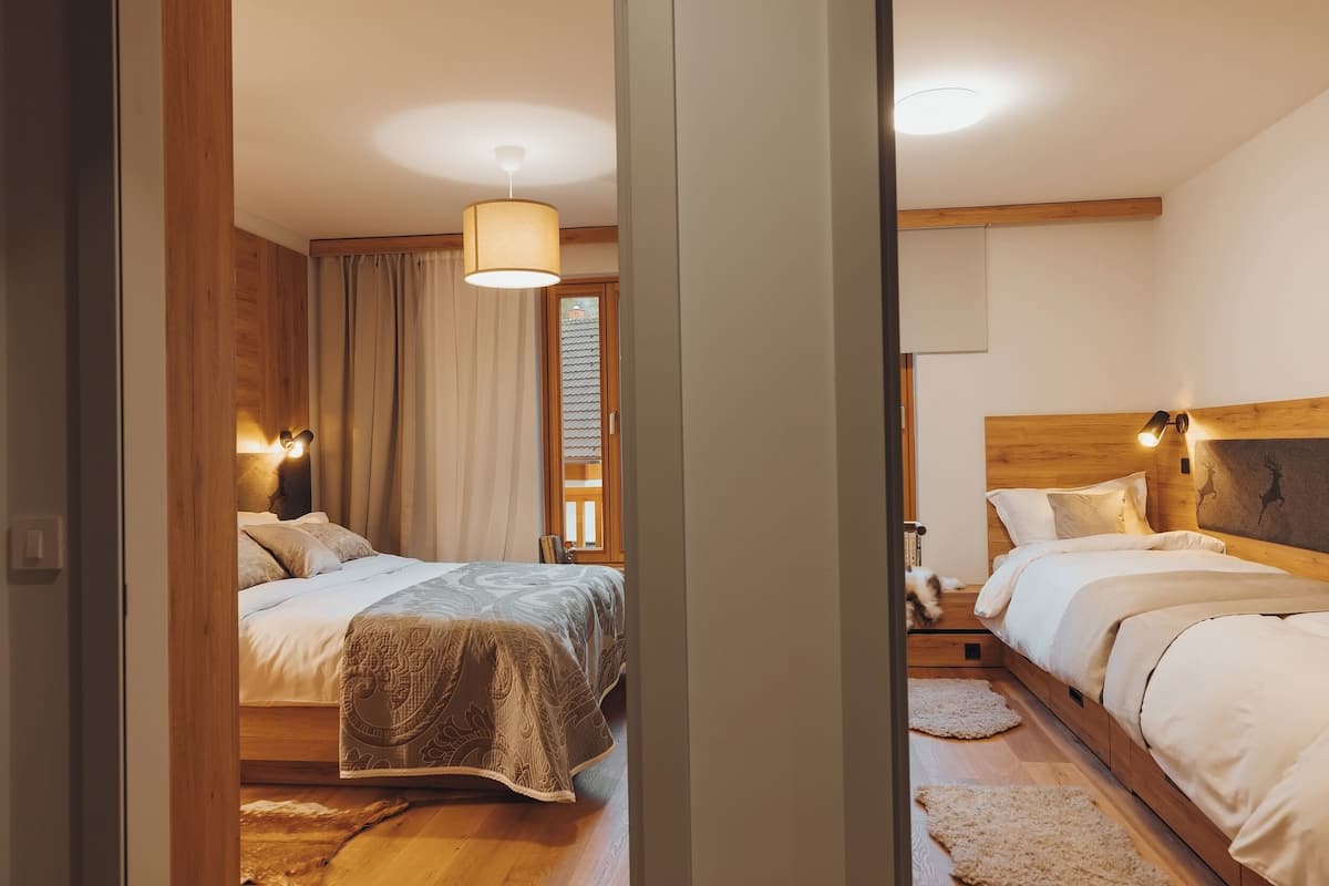 A bedroom with two beds, wooden headboards, and a large window with curtains.