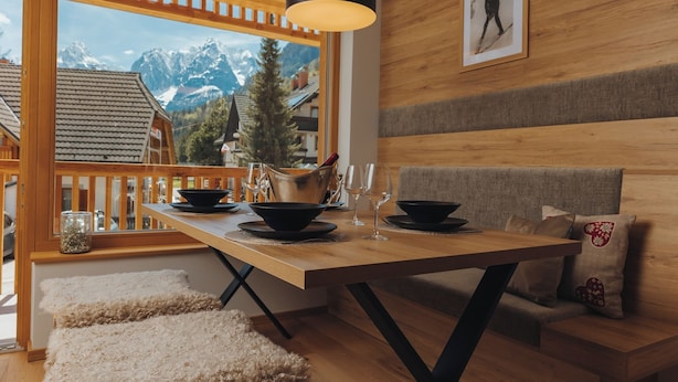 A wooden dining table with black bowls and wine glasses, set against a backdrop of a mountain view through a large window. - Goldhorn Chalet (Kranjska Gora)