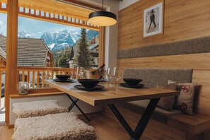 A wooden dining table with black bowls and wine glasses, set against a backdrop of a mountain view through a large window. - Goldhorn Chalet (Kranjska Gora)
