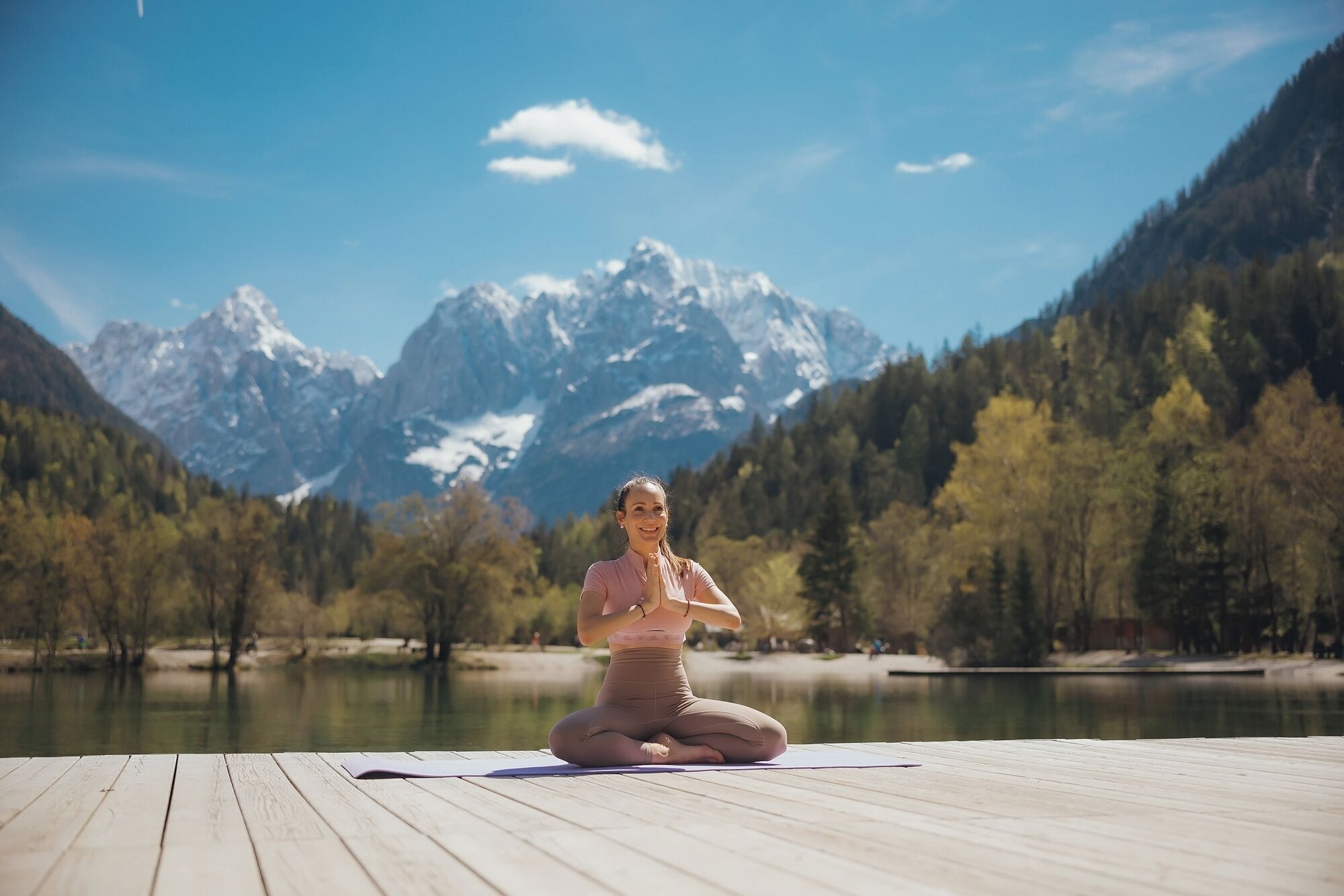 Eine Person sitzt auf einer Holzterrasse mit Blick auf eine Berglandschaft.