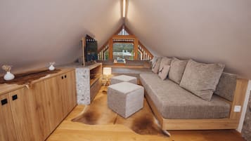 A cozy loft bedroom with a wooden ceiling, a sofa, a small table, and a view of a building through a window.