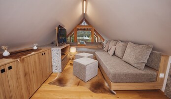 Un dormitorio estilo loft acogedor con techo de madera, un sofá, una mesita y vistas a un edificio a través de una ventana.