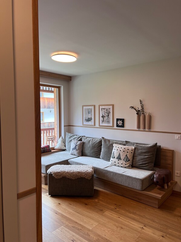 A cozy living room with a grey sofa, a wooden coffee table, and a large window. - Goldhorn Chalet (Kranjska Gora)