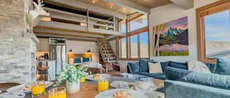 A modern interior with a dining area, a sofa, a painting, and a staircase.
