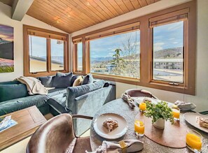A room with a view of a cityscape, a dining table with breakfast items, and a cozy seating area with a couch and chairs.