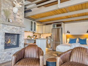 Un interior moderno con chimenea de piedra, sillones de cuero, una cocina con armarios blancos y una cama con almohadas azules.