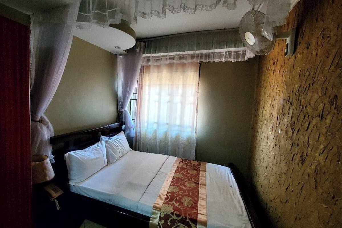 A bedroom with a bed, curtains, a fan, and a wooden wall.