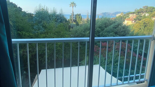Un balcon offrant une vue sur un paysage côtier, avec des arbres et des bâtiments.