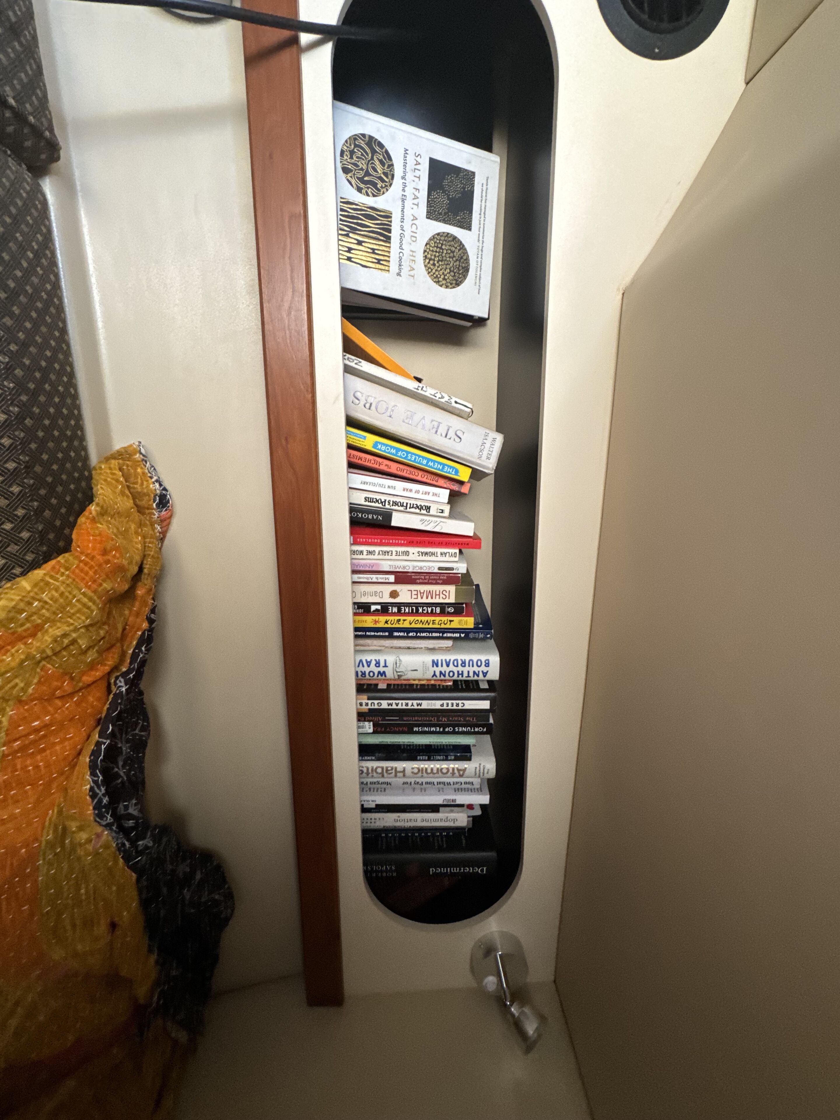 A narrow shelf with a collection of books and a magazine.