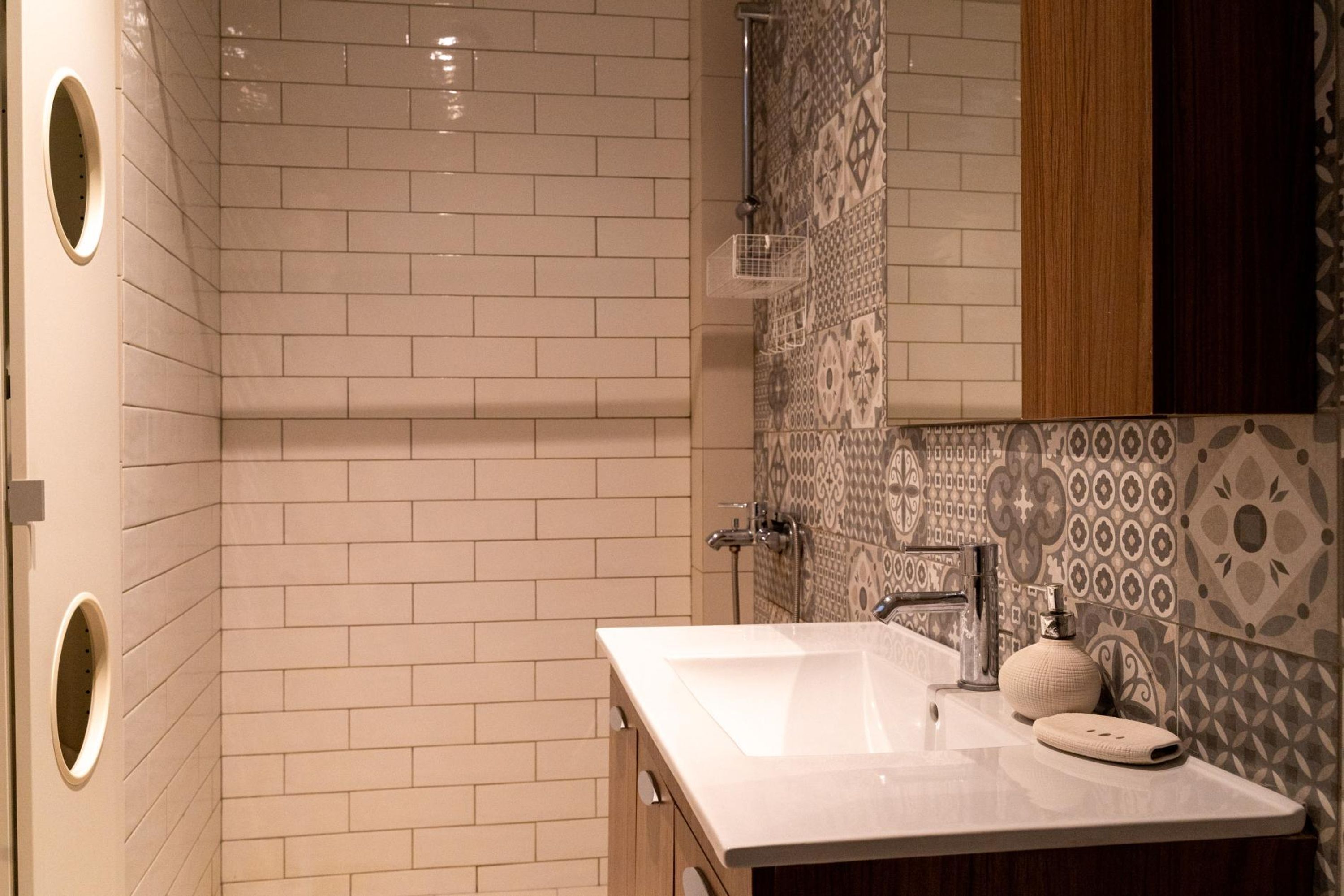 A modern bathroom with a white-tiled shower, a large mirror, and a sink with a soap dispenser.