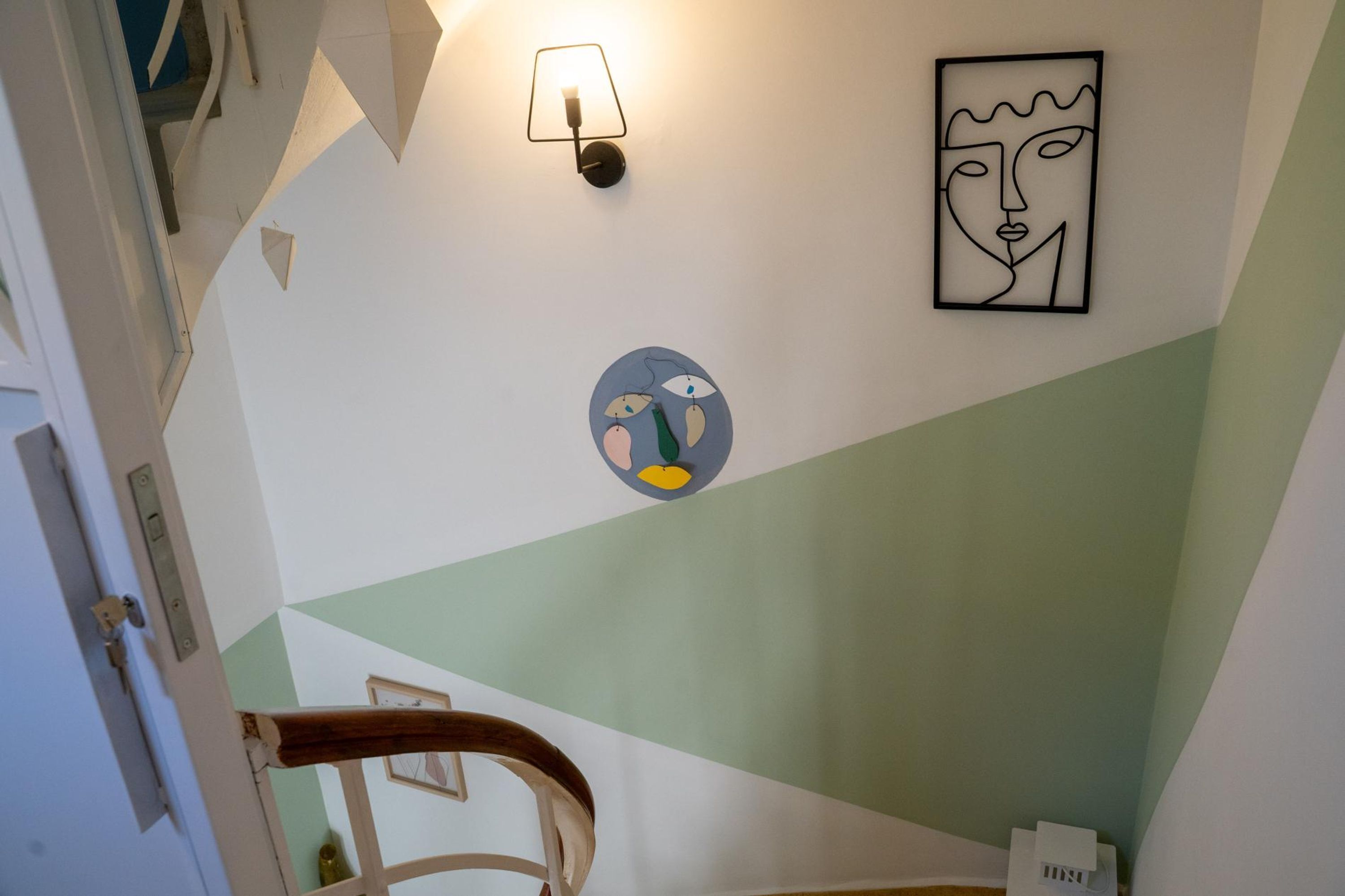 Un escalier avec une rampe, un luminaire fixé au mur et deux œuvres d’art.
