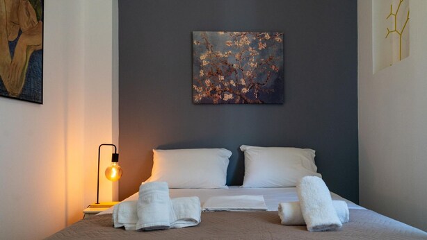 Ein ordentlich bezogenes Bett mit weißen Leinen und Handtüchern, ein Gemälde an der Wand und eine moderne Lampe.
